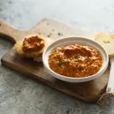 Un bol de poivronade, une recette méditerranéenne savoureuse, servi avec des toasts sur une planche en bois.