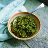 Un bol de pesto de fanes de carottes, prêt à être dégusté, avec une cuillère en argent.