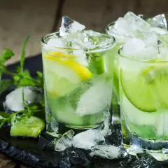 Trois verres de caipirinha glacée, garnie de citron vert et de citron, sur un plateau noir avec de la menthe fraîche. La recette parfaite pour se rafraîchir.