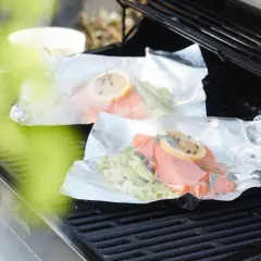 Deux papillotes de saumon en préparation sur un barbecue, prêtes à être cuites.