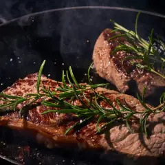 Deux steaks de boeuf Black Angus savoureux, poêlés avec du romarin et du gros sel, dégageant une vapeur alléchante.