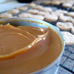 Un pot de confiture de lait onctueuse, prêt à garnir des biscuits secs disposés sur une grille.