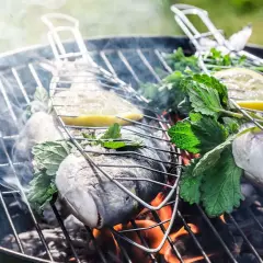 Deux poissons entiers sur un barbecue au charbon, garnis de citron et d'herbes fraîches, fumant doucement. Quel poisson au barbecue charbon !