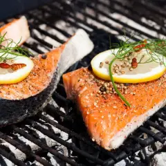 Deux pavés de saumon au barbecue, assaisonnés et garnis de citron et d'aneth, cuisent sur une grille chaude.