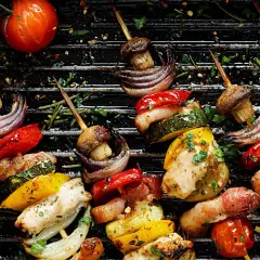 Brochettes de poulet et de legume bbq sur un grill, avec des poivrons, courgettes, oignons rouges, champignons et tomates.