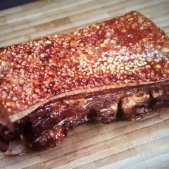 Poitrine de porc barbecue croustillante, avec une couenne dorée et des côtes apparentes, prête à être dégustée sur une planche en bois.