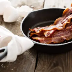 Poitrine de porc fumée, croustillante et dorée, dans une poêle en fonte, avec des œufs et une serviette à côté.