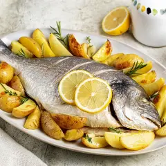 Dorade au barbecue à la portugaise, entière, dorée et savoureuse, accompagnée de pommes de terre rôties et de rondelles de citron.