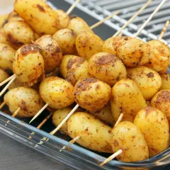 Des brochettes de pommes de terre assaisonnées, prêtes pour le barbecue, dans un plat en verre.