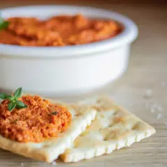 Une cuillère de rillette de chorizo, garnie d'une feuille de persil, sur des crackers. Un bol de cette délicieuse préparation est en arrière-plan.
