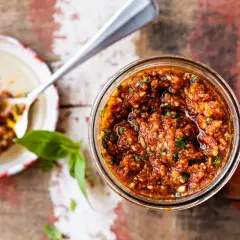 Un pot de pesto rosso, aux tomates séchées et basilic, prêt à être dégusté. Une cuillère en argent en est remplie.