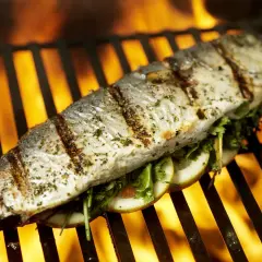 Poisson entier assaisonné, garni de tranches de citron et d'herbes, cuisant sur un gril avec des flammes vives en arrière-plan. Un délice de thon au barbecue.