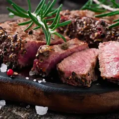 Un succulent filet mignon basse température, coupé en tranches, garni de romarin et de poivre concassé, sur une planche en bois rustique.