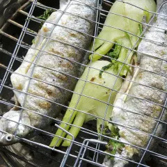 Trois truites entières sur un grill, accompagnées de fenouil, prêtes pour une recette truite barbecue.