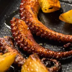Tentacules de poulpe a la plancha, grillés à la perfection, servis avec des quartiers de pommes de terre dorées. Un délice croustillant et savoureux.