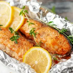 Deux pavés de poisson, cuits en papillote sur la plancha, ornés de rondelles de citron et de brins de thym frais.