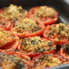 Tomates au barbecue, coupées en deux et garnies d'une chapelure aux herbes, cuites dans un plat.