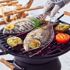 Deux poissons entiers grillent sur un barbecue, accompagnés d'artichauts et de tomates. Un gant tricoté ajuste la grille. Un vrai barbecue hivernal !