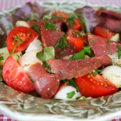 Salade fraîche avec des tranches de fumer magret de canard, tomates, oignons et laitue, parsemée d'herbes.