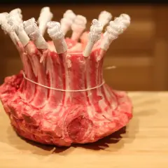 Une couronne d'agneau crue, prête pour la cuisson, avec les os protégés par du papier blanc.