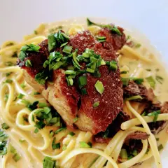 Un morceau d'échine de porc croustillante sur des pâtes crémeuses, garni de ciboule fraîche. Un délice !