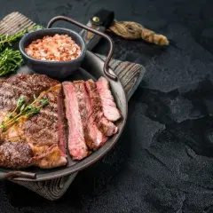 Un succulent entrecôte grillé, tranché et garni de thym frais, servi avec du sel rose sur un plateau.