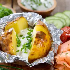 Pommes de terre à la braise, enveloppées dans du papier aluminium, garnies de crème et de ciboulette. Parfait pour le temps de cuisson.