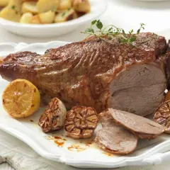 Gigot d'agneau rôti, parfumé au thym, servi avec des citrons grillés et de l'ail confit. Parfait pour une cuisson agneau barbecue réussie.