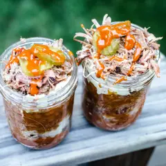 Deux pots en verre remplis de pulled pork, haricots et sauce barbecue, parfaits pour un brunch barbecue en plein air.
