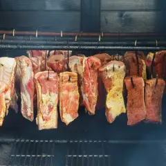 Viande crue assaisonnée suspendue dans un fumoir, prête pour le fumage. Le fumoir est alimenté par une bouteille de gaz.