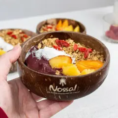 Une main tient un bol en noix de coco rempli d'un délicieux acai bowl, garni de fruits frais, de granola et de baies de goji.