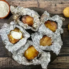 Pommes de terre en papillote sur barbecue, prêtes à être dégustées avec une sauce crémeuse. Le temps cuisson est parfait pour cette recette.