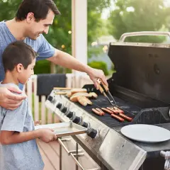 Un père et son fils préparent des saucisses sur un barbecue à gaz. Le père utilise des pinces pour retourner les saucisses pendant que le fils tient un plateau.