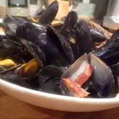 Un plat de moules poulette, fumantes et appétissantes, garnies de lardons croustillants. Un délice à partager.