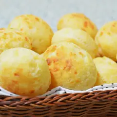 Un panier en osier déborde de délicieux pao de queijo dorés, parfaits pour un goûter.