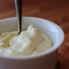 Une cuillère est plantée dans un bol de mayonnaise crémeuse, prête à être dégustée.