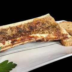 Un os à moelle rôti, assaisonné d'herbes et de poivre, servi avec des toasts croustillants sur une assiette blanche.