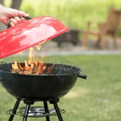 Maintenant, apprenons comment éteindre un barbecue. Une main soulève le couvercle rouge d'un barbecue noir où des flammes dansent.