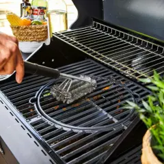 Main d'homme utilisant une brosse métallique pour nettoyer la plaque du barbecue.