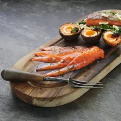 Tranché de truite fumée, œufs panés et garniture sur planche en bois. La cuisson truite fumée est mise en valeur.