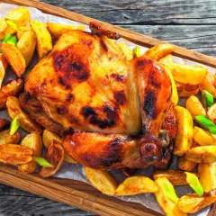 Un poulet rôti doré et croustillant, entouré de pommes de terre rôties et d'oignons verts, prêt à être dégusté.