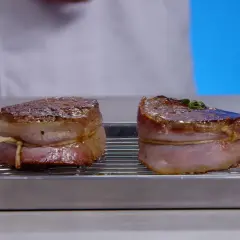 Deux filets mignons au barbecue, enveloppés de lard, reposent sur une grille dans un plat.