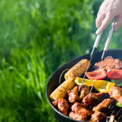 Un barbecue sain en plein air avec des épis de maïs, des poivrons colorés et des brochettes de poulet grillant sur le feu.