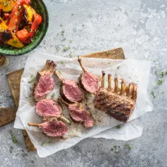 Un délicieux carré d'agneau au barbecue, coupé en côtelettes rosées, servi avec des poivrons grillés.