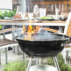La grille bbq est prête pour un festin en plein air. Des flammes dansent sur les braises, promettant des saveurs estivales. La table est dressée, invitant au partage.