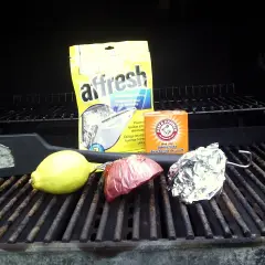 Sur la grille barbecue, un citron, un oignon, du papier aluminium, un nettoyant pour lave-vaisselle et du bicarbonate de soude.