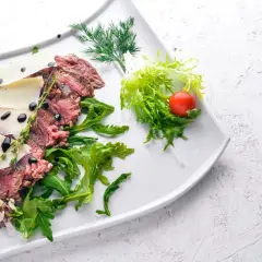 Délicieuse tagliata de boeuf, finement tranchée, garnie de copeaux de parmesan, de roquette fraîche et d'une touche de vinaigre balsamique.