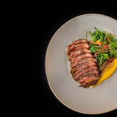 Tranches de rumsteak d'agneau grillé, servies avec une purée de courge et une salade fraîche.