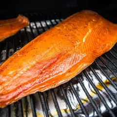Deux filets de saumon orangés, assaisonnés de poivre, reposent sur une grille. Le temps de fumage à froid est presque terminé.