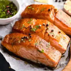 Trois pavés de saumon fumé, parsemés de poivre, accompagnés d'une sauce verte et d'une tête d'ail. Une recette parfaite pour une marinade pour saumon fumé.